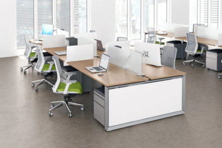 Studio photography of AMQ's Icon Benching. There is two 2-Pack double run workspaces, each with a green cushioned chair placed at the desk. The sun is shining in from the window beyond.