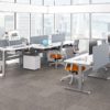 KINEX Studio Shot Showing some double and single run workspaces by the window. Sunlight shines on the white laminate desk top.