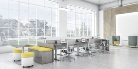 Global's 6-person power beam desks in an office space with tall ceilings. Each workstation has a laptop open, with glass paneling for privacy. Sunlight is cast upon the acoujou finish. At one end is a cabinet with sunflower yellow cushions, and a square Swap table.