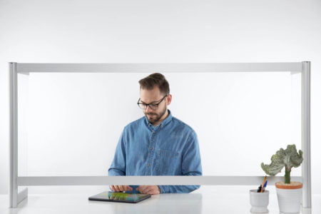 A man stands behind a counter, looking at his tablet. A Counter Shield Wrap model screen separates him from the space in front.