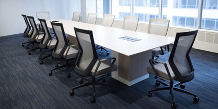 Twelve Run II chairs placed at a long conference table. Each chair has a grey mesh back with matching cushion. Windows overlook the city street, letting light into the room.