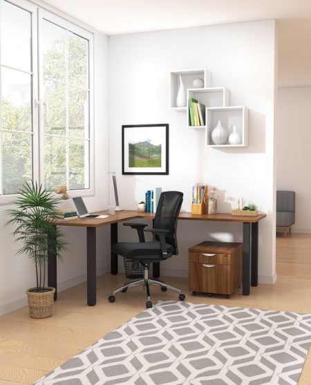 Studio shot of OTG's Home Office, with an L-shaped desk placed by the window. It has a black colored metal frame and top surfaces in a Autumn Walnut finish. A matching set of drawers has been rolled under the desk, by a set of pencil cases. The office chair is seated by a laptop and an OTG LED Desk lamp in the corner.